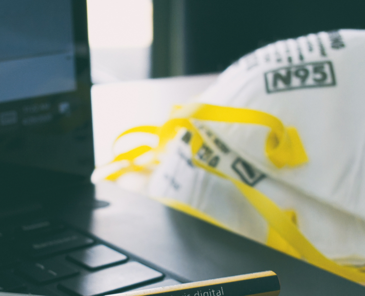 An image of a laptop, N95 face masks and a pencil in the foreground